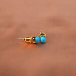 Close-up of turquoise stone set in gold-plated posts showing texture