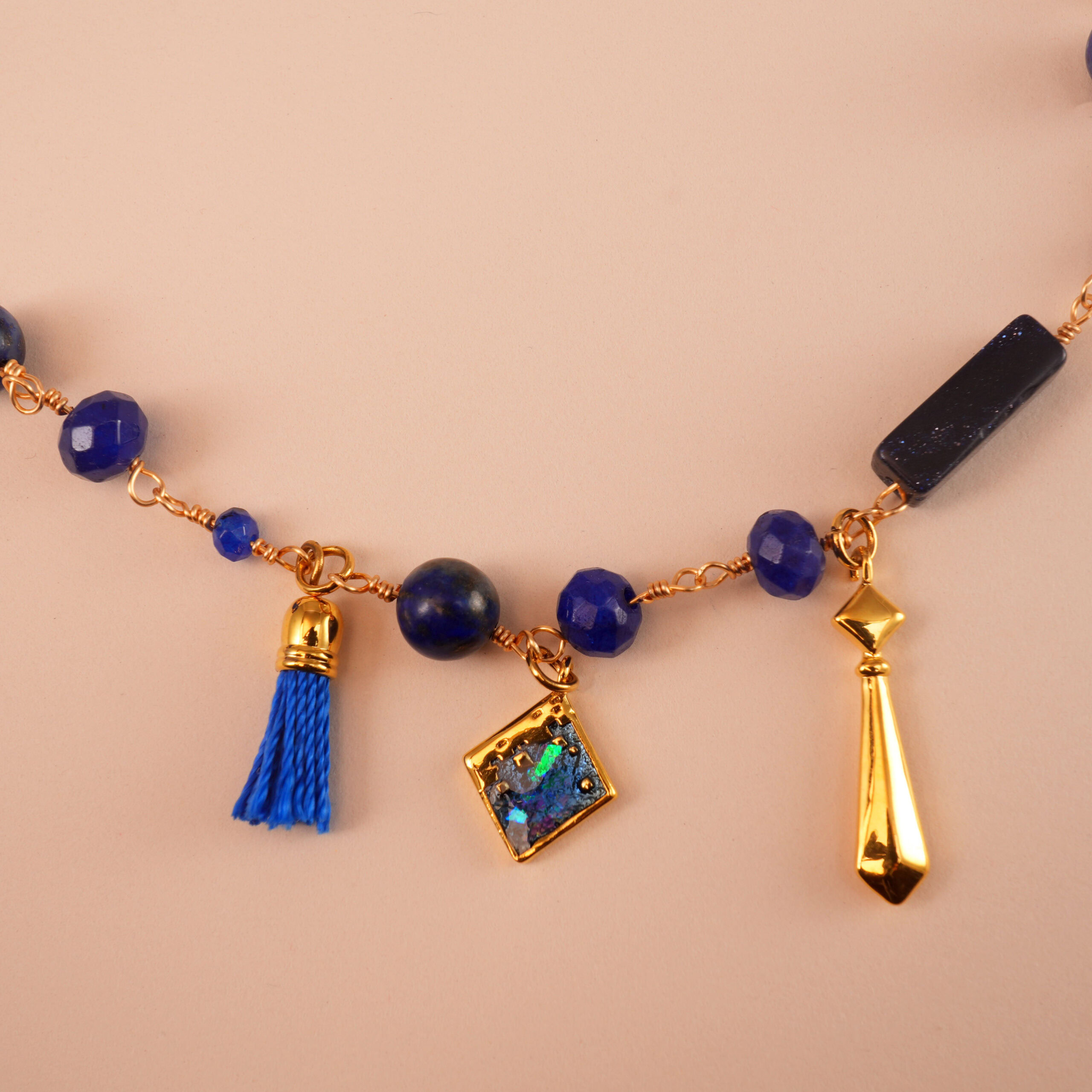 lapis-lazuli-charm-necklace-detail "Close-up of Lapis Lazuli charm necklace showcasing intricate gold pendants, vibrant beads, and tassel detail."