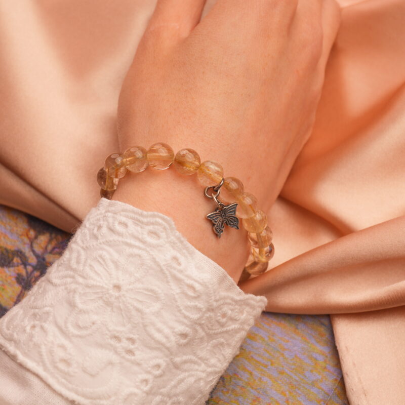 Golden rutilated quartz charm bracelet worn on wrist in natural light