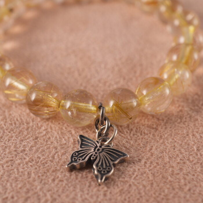 Close-up of golden threads inside rutilated quartz beads and butterfly charm