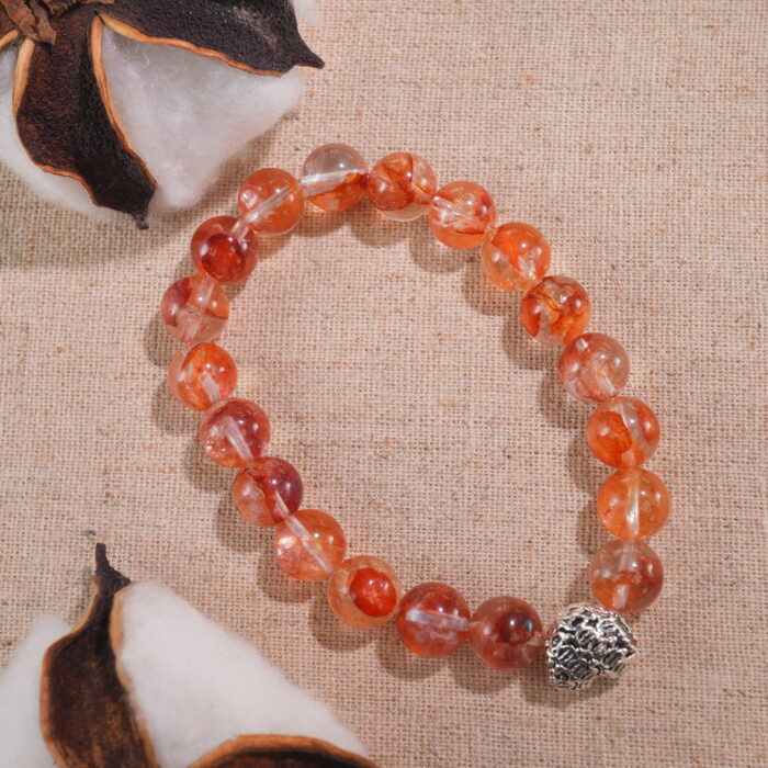 Heart bracelet with red jelly opal placed beside dried flowers – vibrant energy scene