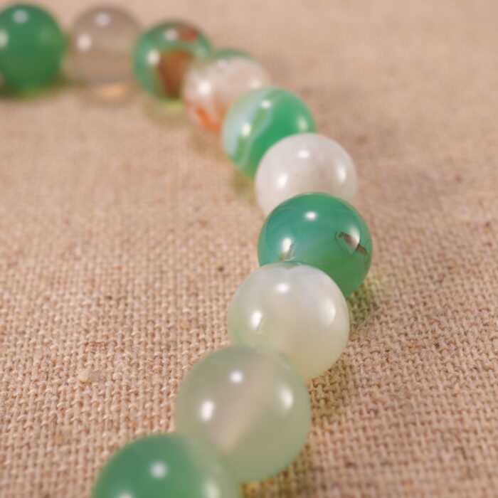 Close-up view of the polished agate beads and heart charm on the bracelet, showing texture and natural color.