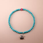 Close-up of a handcrafted turquoise and rhodochrosite bracelet with fish charm on white background