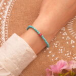 Model wearing turquoise and rhodochrosite charm bracelet with fish pendant on wrist