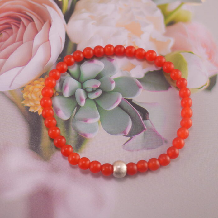 Carnelian and red agate bracelet placed beside flowers and crystals – vibrant and energizing