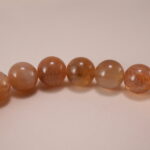 Close-up of smooth 6mm peach moonstone beads and charm detail