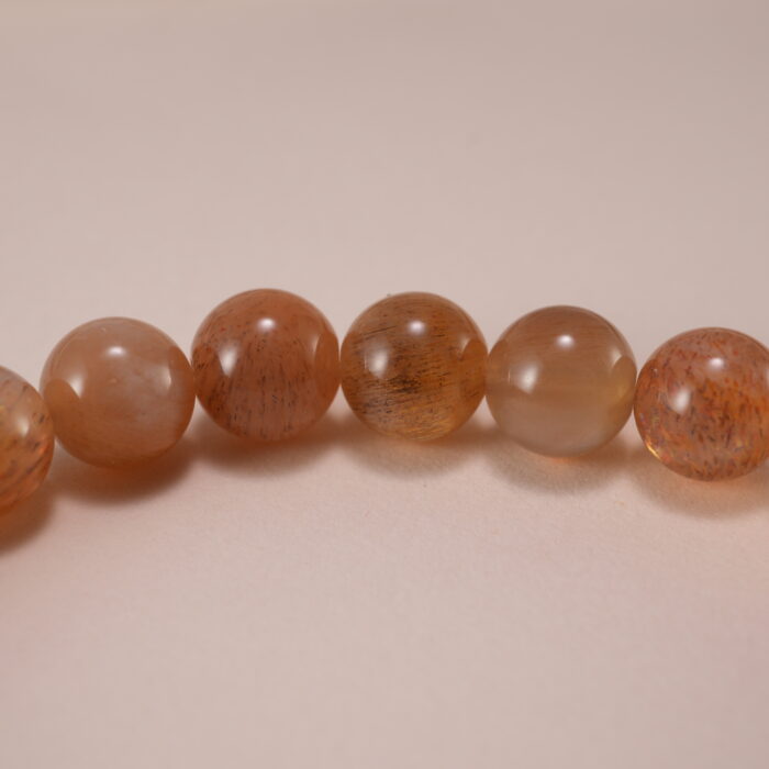Close-up of smooth 6mm peach moonstone beads and charm detail