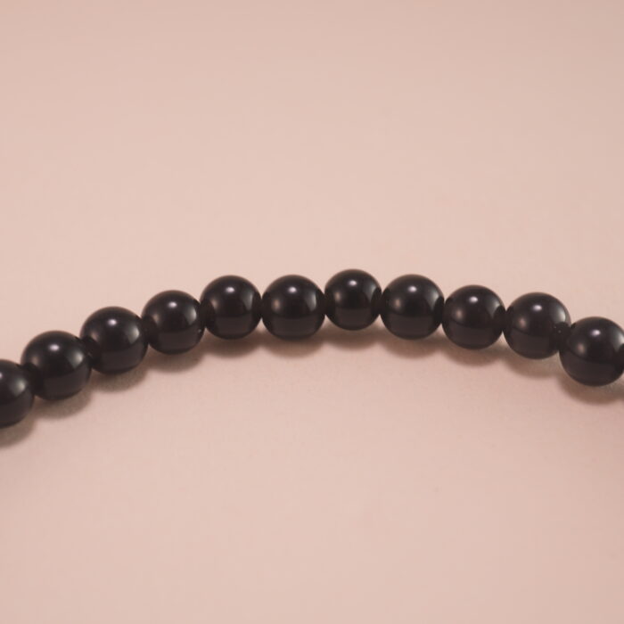 Close-up of the obsidian and turquoise beads, gold clasp, and silver charm detailing