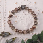 Bracelet resting gently beside the green leaf in natural sunlight, evoking warmth and calm