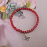 Red agate butterfly charm bracelet placed near flowers – symbol of energy and growth