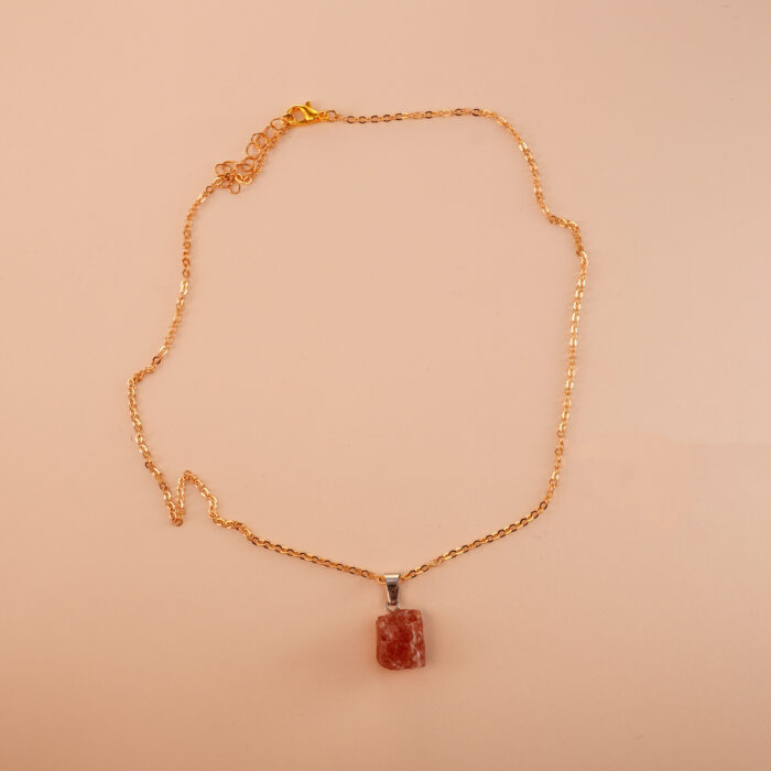 Handmade rose quartz pendant necklace displayed on neutral fabric background
