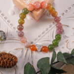 Agate bracelet resting on a neutral fabric with green leaves nearby – natural and calming scene for a colourful heart bracelet