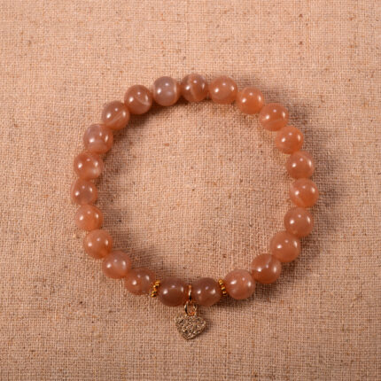A delicate peach moonstone bracelet with a silver heart charm centered