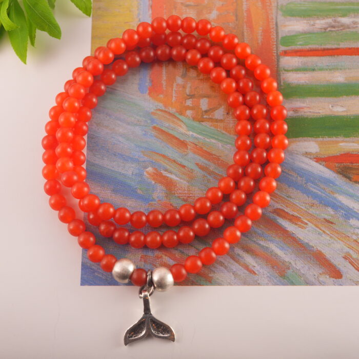 Red agate silver charm bracelet displayed with natural and warm-toned props