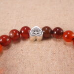 Close-up of red agate beads and silver heart charm on elastic cord