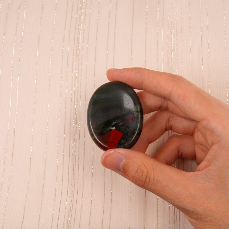 Hand gently holding the African Bloodstone worry stone, showcasing its smooth surface and colors