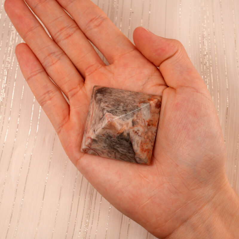 Person holding a Natural Crazy Agate Pyramid Decoration, showcasing its unique patterns and vibrant colors.