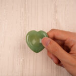 Hand holding a green aventurine heart-shaped crystal between thumb and forefinger
