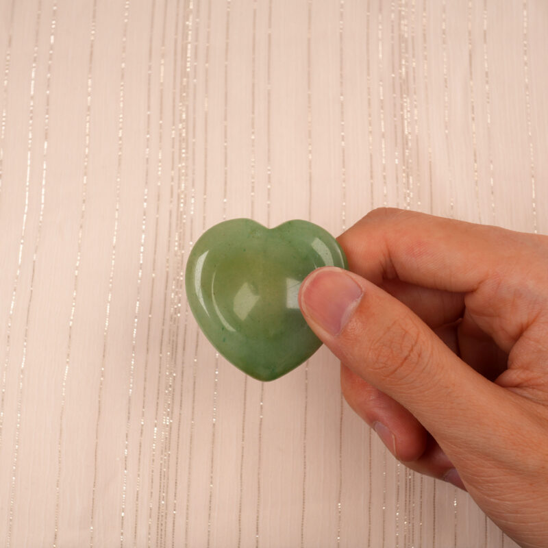 Hand holding a green aventurine heart-shaped crystal between thumb and forefinger