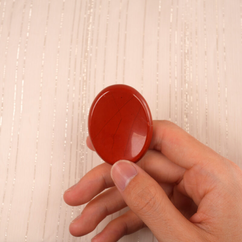 Hand holding a Red Jasper worry stone, showcasing its size and vibrant red color
