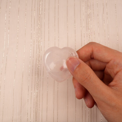 Fingers gently pinching a small Rose Quartz heart crystal against a neutral background
