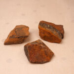 Natural Tiger Eye raw stones displayed on a neutral background, showing golden-brown bands and rough textures.