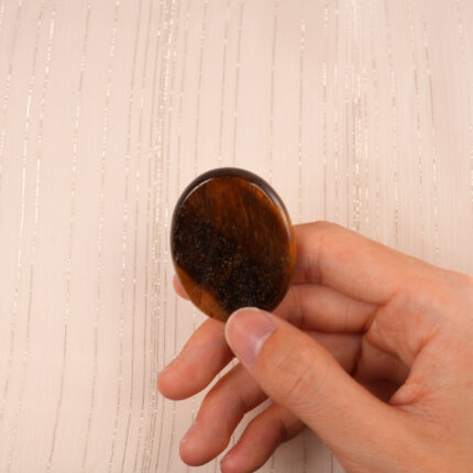 Hand holding a polished Tiger Eye worry stone, showcasing its size and natural shine