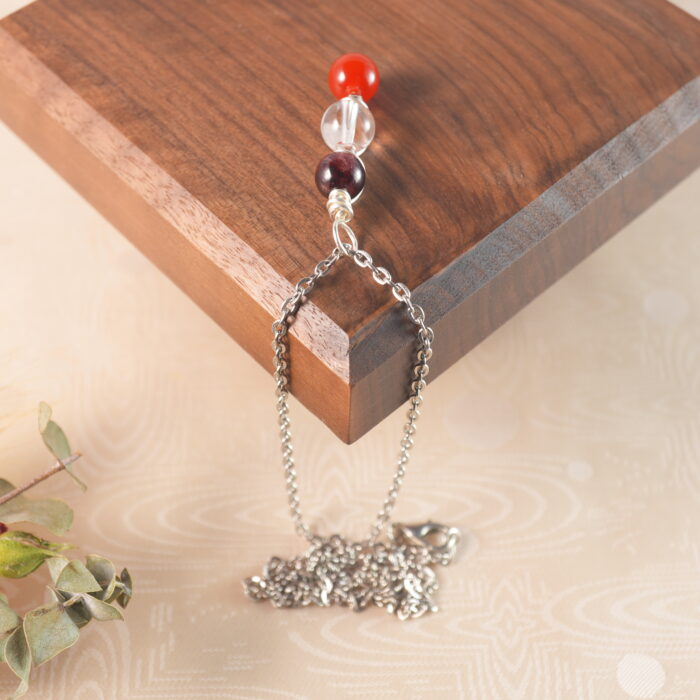Aries zodiac necklace displayed on wooden board with amethyst, clear quartz, and red agate.