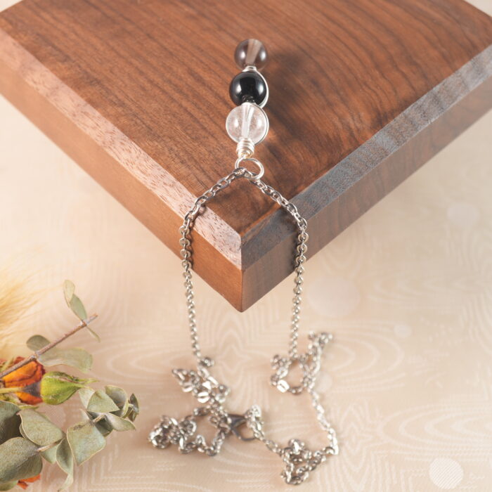 Capricorn zodiac necklace displayed on wooden board with clear quartz, obsidian, and smoky quartz.