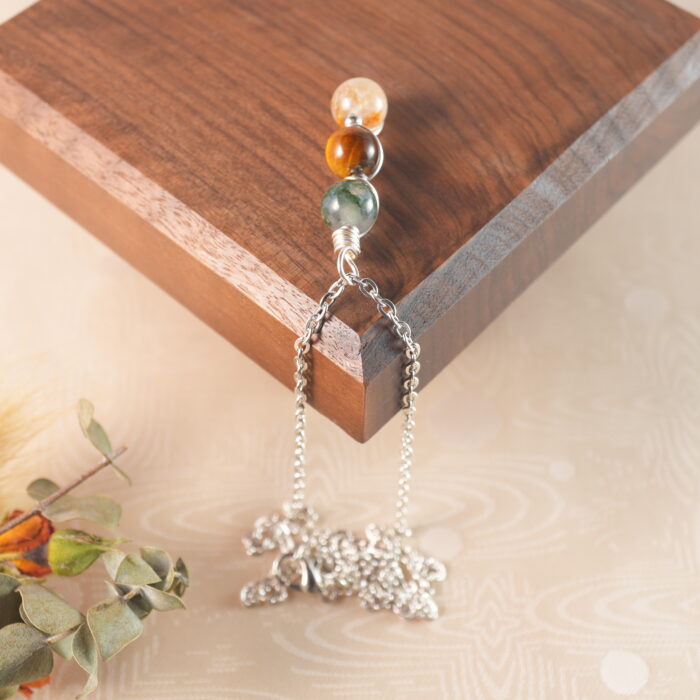 Gemini zodiac necklace displayed on wooden board with moss agate, tiger eye, and citrine.