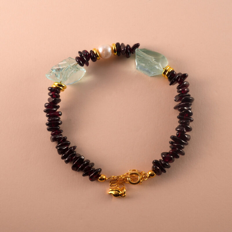 Handmade Aquarius-themed bracelet featuring garnet, pearl, and aquamarine beads laid out in a minimalist design.