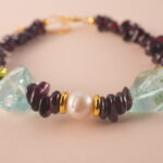 Close-up of polished garnet, lustrous pearl, and translucent aquamarine beads strung on durable elastic cord.