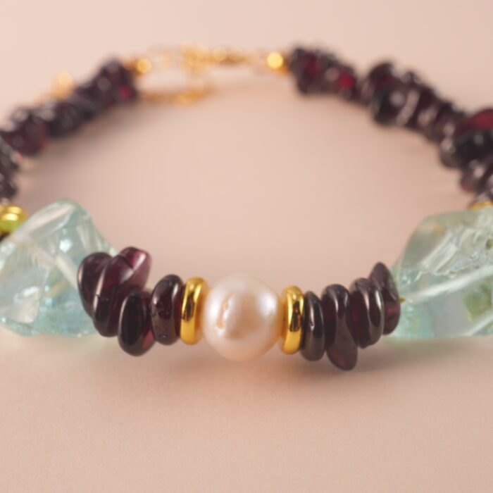 Close-up of polished garnet, lustrous pearl, and translucent aquamarine beads strung on durable elastic cord.