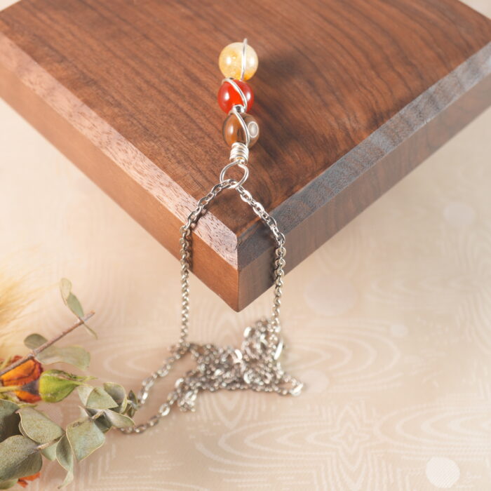 Leo zodiac necklace with tiger eye, red jasper, and citrine displayed on wooden board.