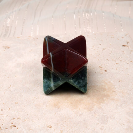 Polished natural Indian Agate Merkaba ornament featuring deep green and earthy red tones, displayed on a stone-textured surface.