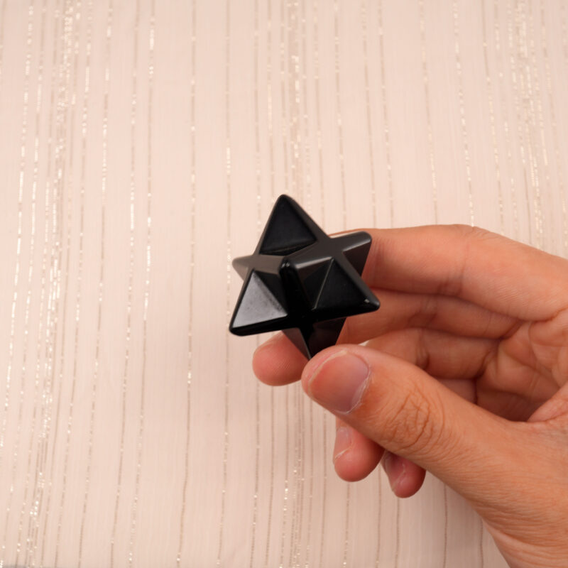 Hand holding a smooth Obsidian Merkaba crystal to show its size and polish.