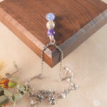 Pisces zodiac necklace displayed on wooden board with amethyst, crazy agate, and aquamarine.