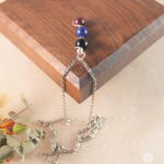 Scorpio zodiac necklace displayed on wooden board with obsidian, lapis lazuli, and garnet.