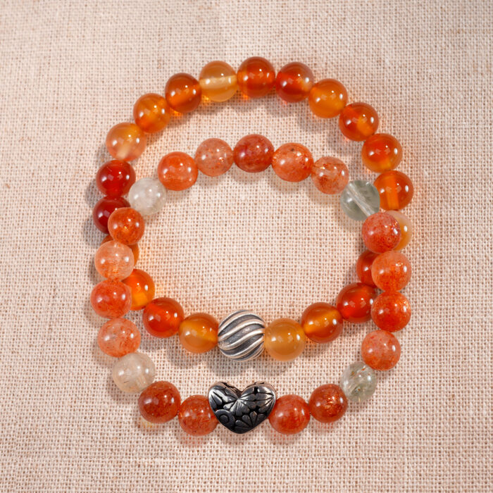 Flatlay of stacked bracelets featuring Arusha sunstone and flower red agate.