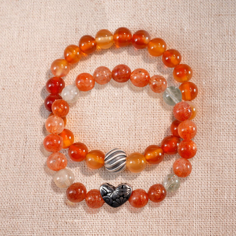 Flatlay of stacked bracelets featuring Arusha sunstone and flower red agate.