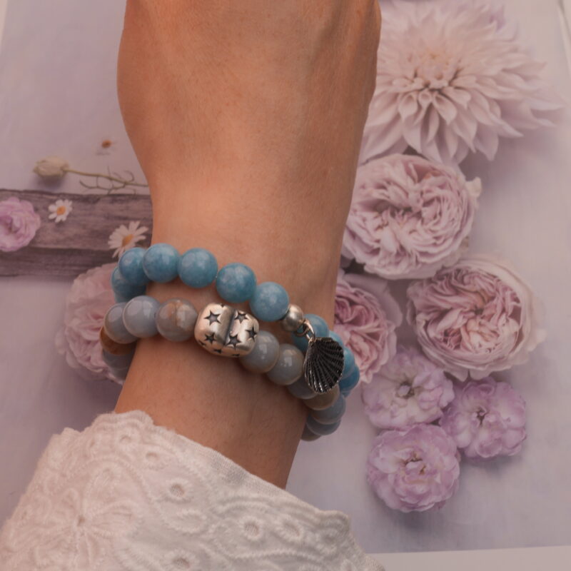 Model wearing stacked blue and cream chalcedony bracelets on wrist.