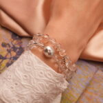 Model wearing stacked bracelets of clear and rutilated quartz with silver highlights.