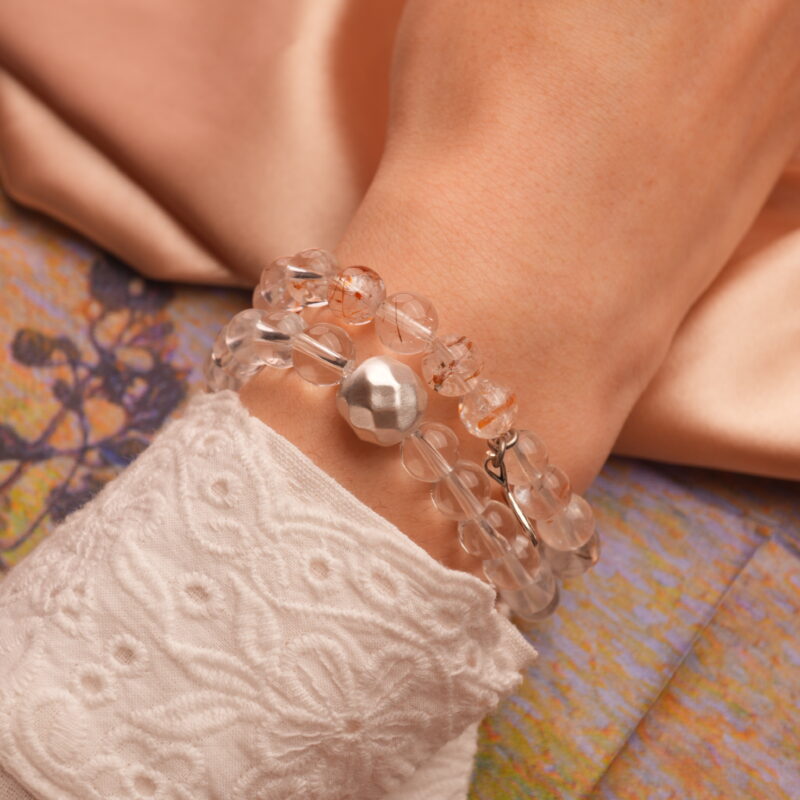 Model wearing stacked bracelets of clear and rutilated quartz with silver highlights.