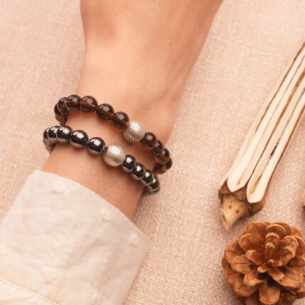 Model wrist wearing stacked hematite and smoky quartz bracelets.