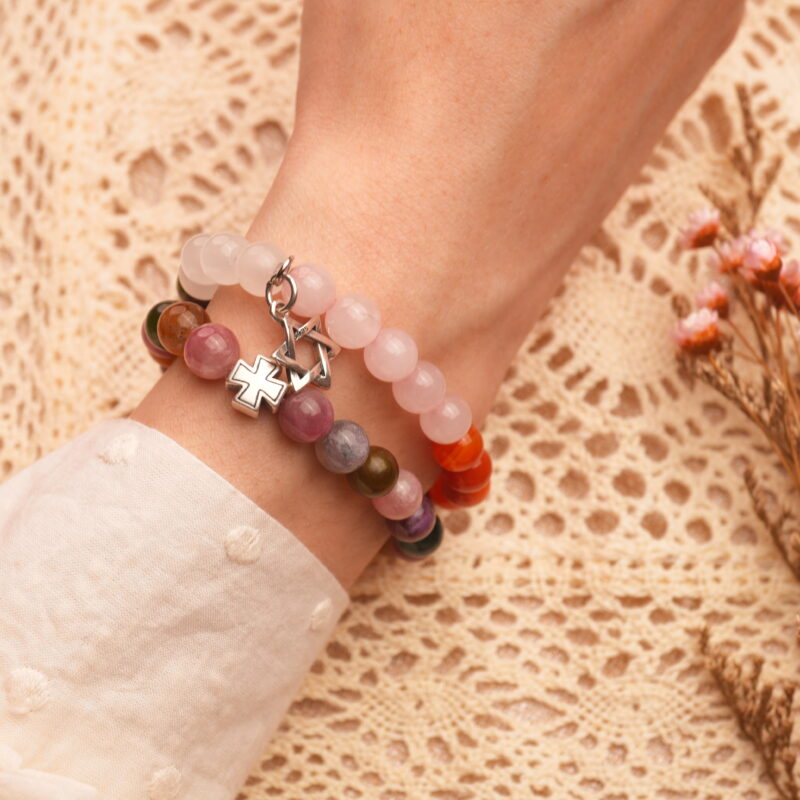 Model wearing stacked bracelets with pink, green, and dark tones.