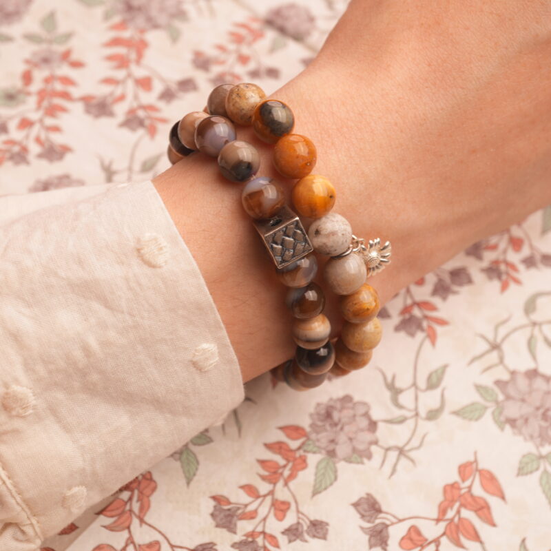 Model wearing stacked earthy and cool-toned gemstone bracelets.