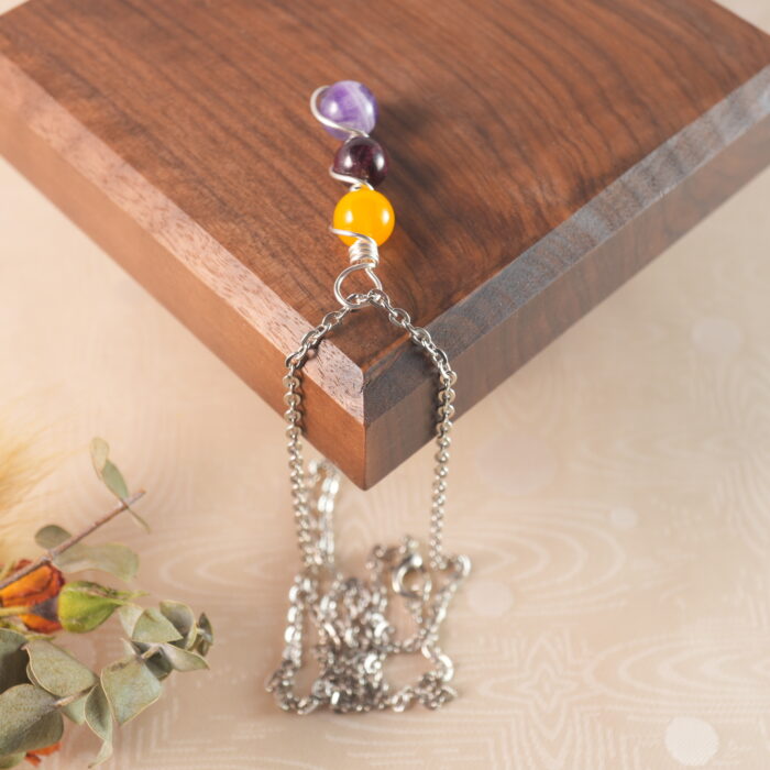 Virgo zodiac necklace displayed on wooden board with yellow agate, garnet, and amethyst.