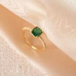 Adjustable open emerald ring placed on a clean backdrop, featuring a vivid green stone and a sleek silver band.