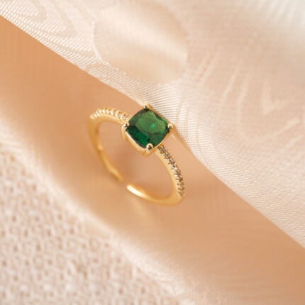 Adjustable open emerald ring placed on a clean backdrop, featuring a vivid green stone and a sleek silver band.