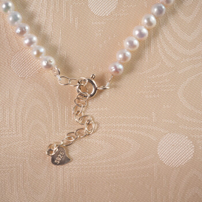 Detailed view of the adjustable pearl necklace's clasp and chain mechanism, showing pearl texture and adjustable features.